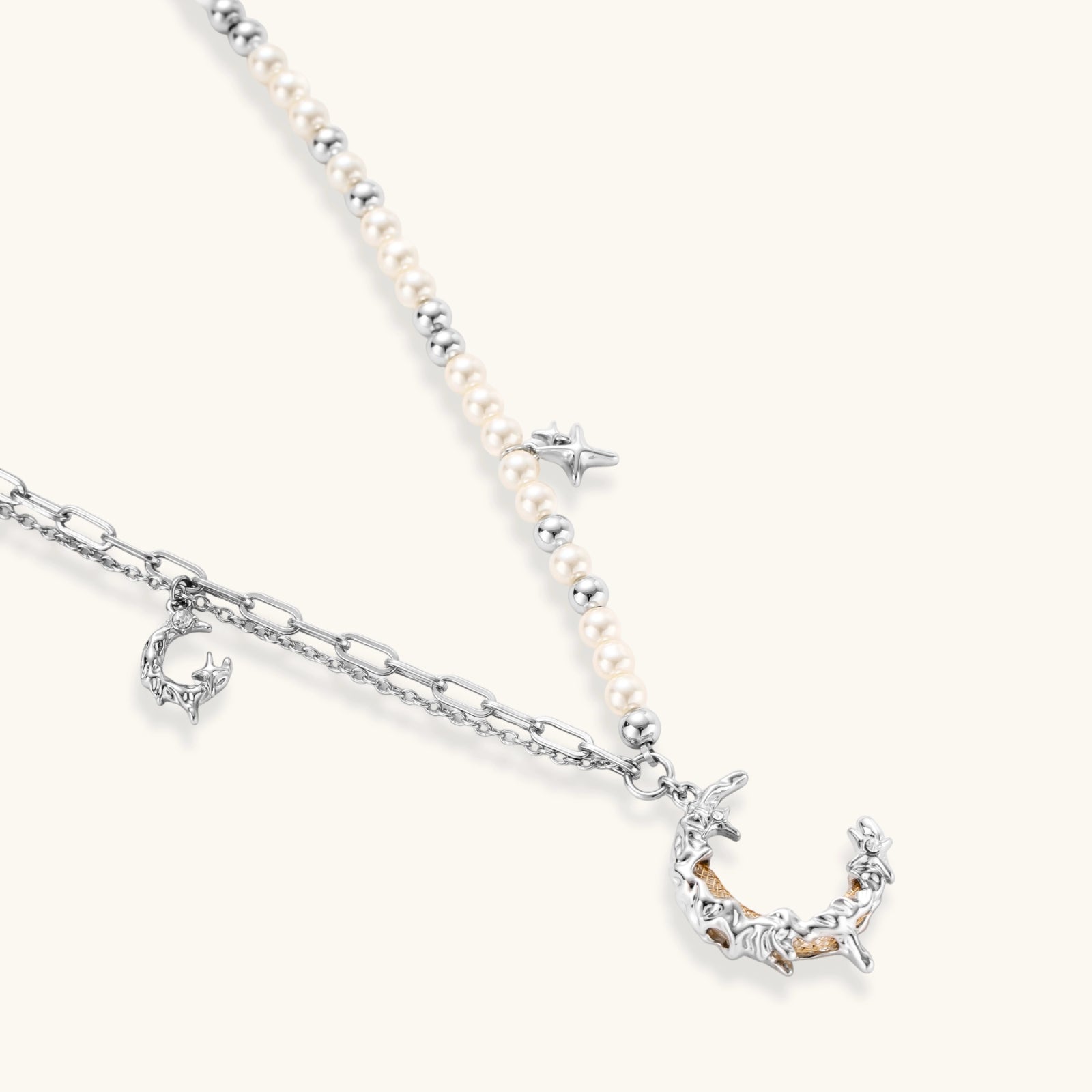 Silver-toned crescent moon pendant with star accents on pearl and chain necklace against white background.